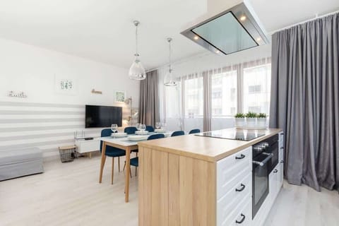 The open-plan kitchen features white cabinets, a wooden countertop, and modern appliances, seamlessly connected to a dining area with a sleek table and blue chairs.