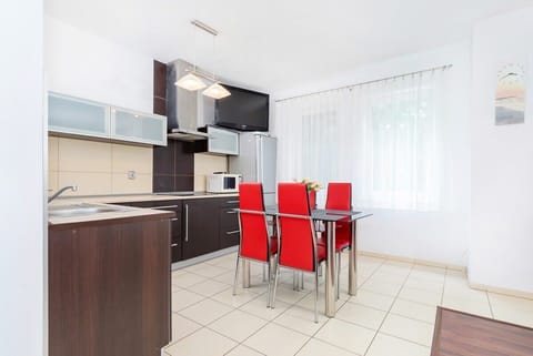 The dining area features a table with red chairs. The kitchen is equipped with dark cabinets and stainless steel appliances.