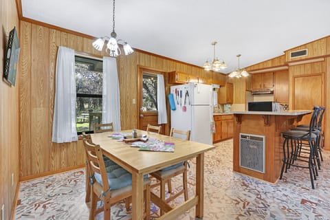 View of the dining table and kitchen as you walk from the entry door. The backdoor of the home that leads to the backyard can be seen to the left of the refrigerator.
