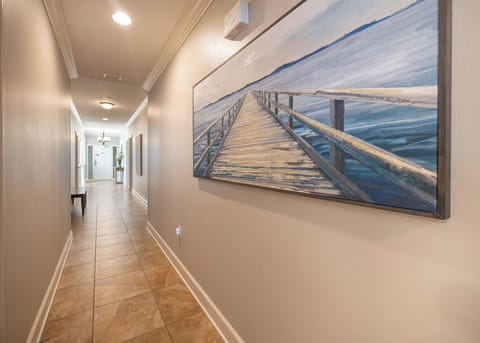 This hallway features a serene coastal painting, warm tile flooring, and leads to inviting spaces beyond