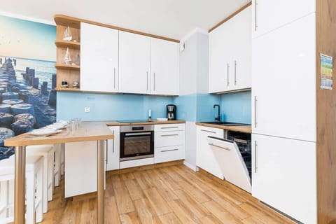 A compact kitchenette with white cabinetry, a blue backsplash, and modern appliances like an oven and fridge.