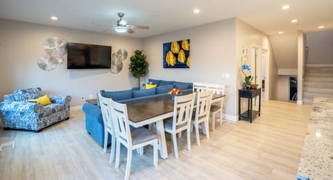 UNIT A (4Bdrm): The living room boasts a captivating blue aesthetic and is outfitted with a Smart TV. Ample seating arrangements invite family and friends to gather around the television, while the open layout seamlessly connects to the kitchen, ensuring everyone can enjoy each other's company.
Dining table for 6 guests, plus bar stools at the nearby kitchen island.