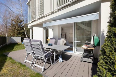 A well-furnished terrace with a table, chairs, and a parasol, surrounded by a green garden.