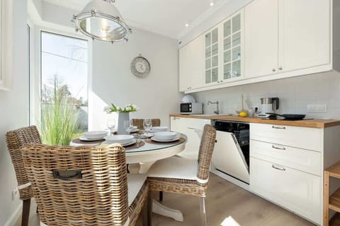 Dining table and chairs in a well-lit living room, styled for a meal. A functional kitchen featuring white cabinets and green plants as decor.