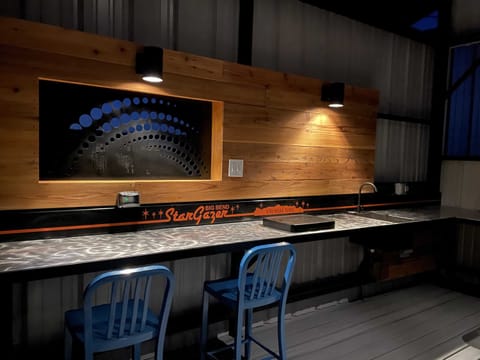 Outdoor kitchen is well lit with dark sky friendly lights. Blue chairs define the computer station with outlets and USB charge ports mounted on the wall.