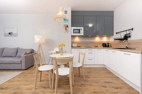 A bright, open-plan living room with a dining area in the background, featuring wooden floors, modern furniture, and soft lighting.