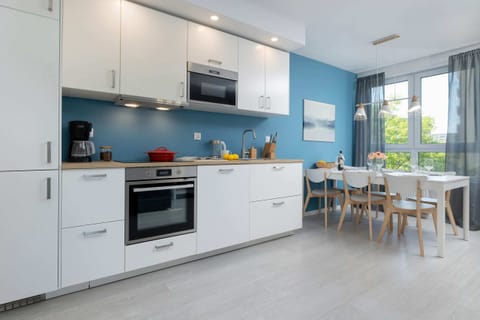 A fully equipped kitchen with blue walls, white cabinets, and a nearby dining table.