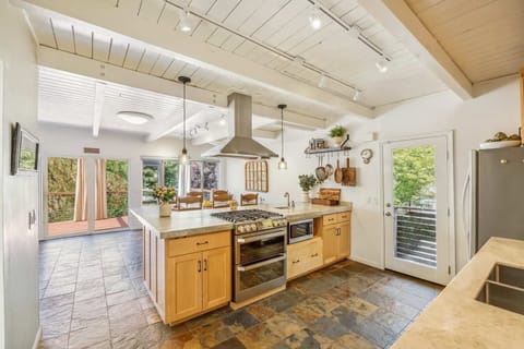 A warm, beautifully lit kitchen with natural wood cabinets and a large central island. Sliding doors open to the deck, making cooking, dining, and entertaining feel effortless.