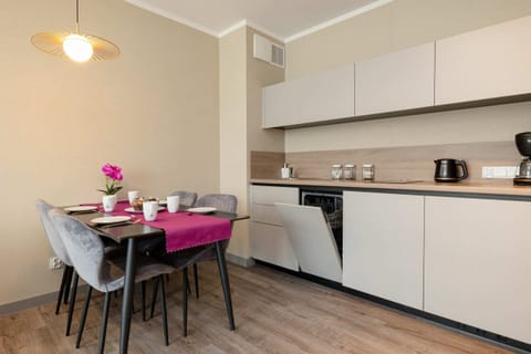 A fully equipped modern kitchenette with white cabinetry, alongside a dining table with upholstered chairs.