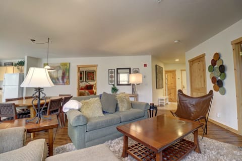 A cozy living room with a green sofa, wooden coffee table, tan butterfly chair, and modern decor. The room features a mix of contemporary and rustic elements, with art on the walls and a shag rug.
