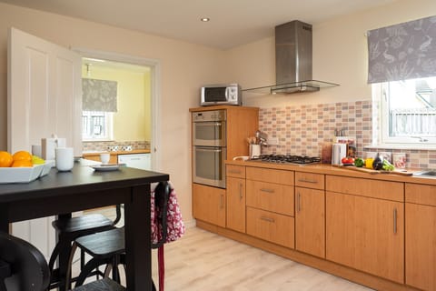 Modern kitchen with electric oven, gas hob, microwave and coffee maker.
