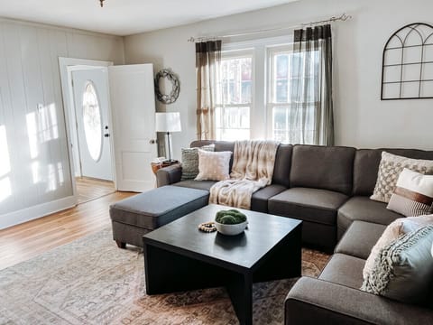 Living room with sectional sofa and soft throw blankets - Bright windows and modern wall decor create cozy style - Spacious spot to relax and enjoy quality family time