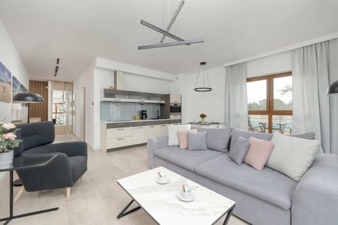 A bright and modern living room featuring a light gray sofa, a sleek black armchair, and a coffee table, with large windows letting in abundant natural light.