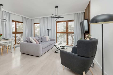 A bright and modern living room featuring a light gray sofa, a sleek black armchair, and a coffee table, with large windows letting in abundant natural light.