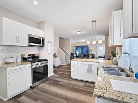 White kitchen boasts granite counters, island workspace under pendant lights, stainless gas range, and a sleek sink. Open layout flows seamlessly into the living area—perfect for cooking & socializing! 🍳✨🏠