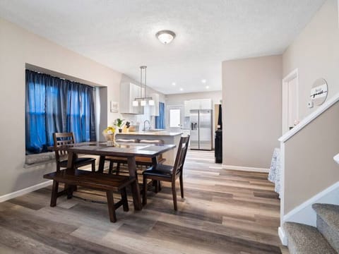 Cozy open space with leather sofas, wooden coffee table, and adjacent dining bench and chairs by bay window. Vinyl plank floors and blue curtains add warmth and style—perfect for relaxing and entertaining! 🛋️🍽️🏠