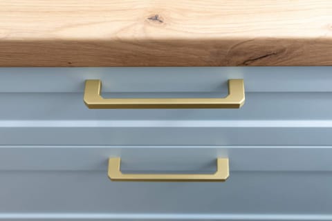 Close-up of a blue drawer with gold handles and wooden texture.

