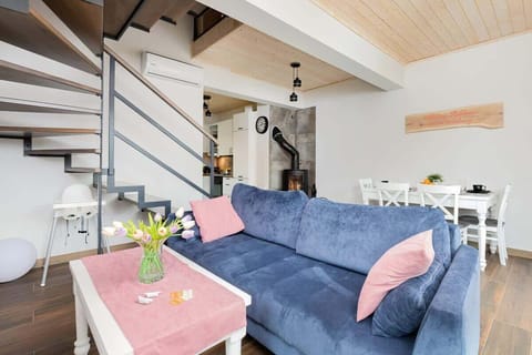 A cozy living room with a blue sofa, a pink throw blanket, and a small coffee table, decorated with flowers.