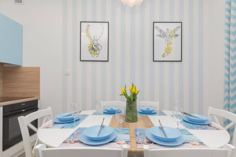 A dining table set with blue tableware and fresh flowers in a vase, placed in a bright area between the living room and kitchen, perfect for meals.
