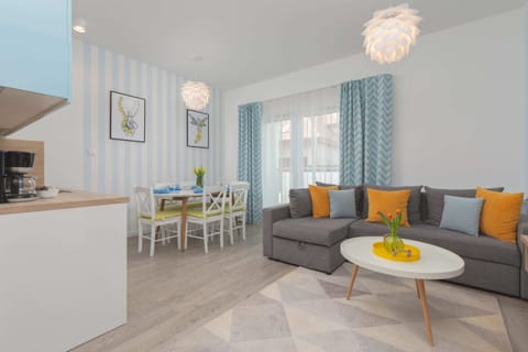 A modern living room featuring a cozy gray sofa, bright yellow cushions, and a sleek TV mounted on the wall. The large window allows plenty of natural light to brighten the space.