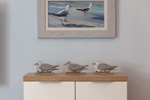 A wooden sideboard against a white wall, adorned with a framed picture, small plants, and a nautical-themed decoration.