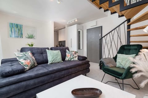 A cozy living area featuring a grey sofa, green armchair, and wooden staircase. The space is decorated with modern furniture and accents.