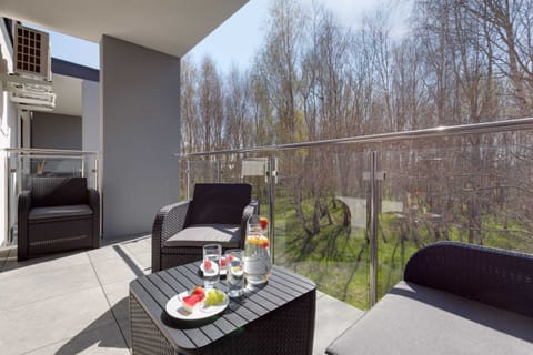 A balcony furnished with a table and chairs, offering a scenic view of trees and greenery.