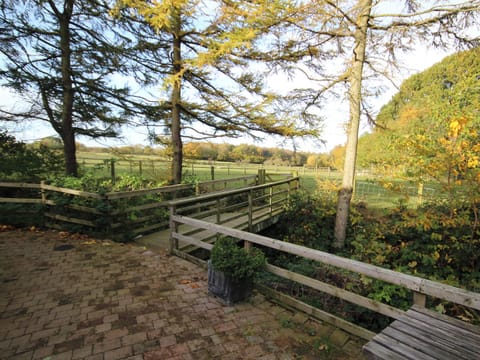 Paved patio with views through the trees to the play field and countryside beyond | Nuthatch Cottage - Wallace Lane Farm Cottages, Brocklebank, near Caldbeck and Uldale