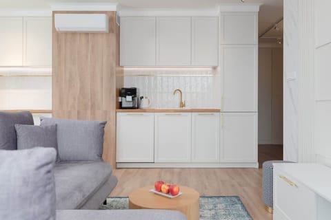 A compact yet functional kitchen with white cabinetry and gold fixtures. The design incorporates light wood accents for a modern and warm touch.
