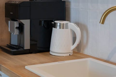 A close-up of a coffee machine and kettle on a light wood counter, reflecting the kitchen's clean, functional design.