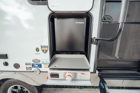 The outdoor kitchen is equipped with a mini refrigerator, spray port, & griddle