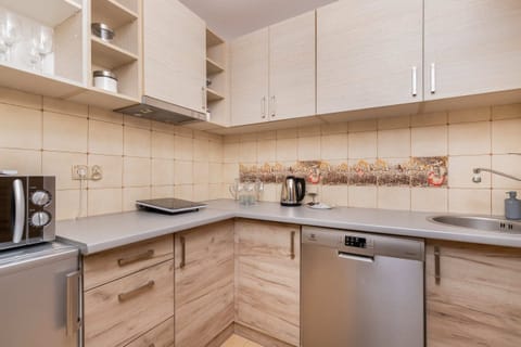  A compact kitchen featuring wooden cabinets, a tiled backsplash, and stainless-steel appliances. The design combines functionality with a natural look.