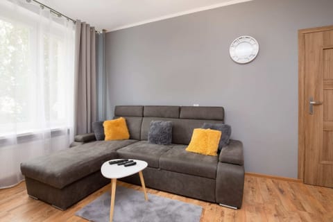 A cozy living room with a grey sofa, yellow accent pillows, and a round coffee table. Wooden flooring and neutral walls create a warm ambiance.