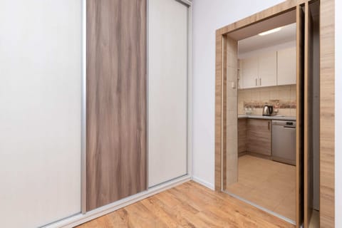 A simple hallway with a warm wooden floor and a door leading to other parts of the apartment. The neutral tones create a welcoming feel.