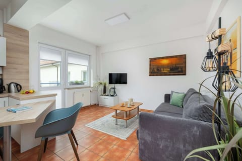 A wide shot of the living room with a gray couch, wooden coffee table, and a painting on the wall. The kitchen and dining areas are visible in the background.