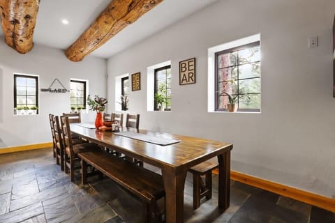The dining area is just off of the living room and features a spacious dining table with chairs and benches that can seat up to 19, rustic log beams, and ample natural light.