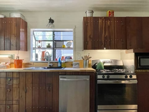Fully equipped rustic kitchen with wooden cabinets, stainless steel appliances, and a bright window above the sink.