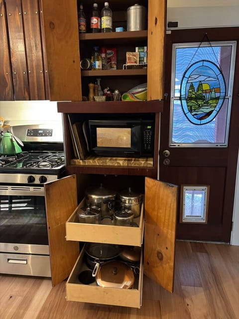 Functional kitchen corner with stove, microwave, and pull-out drawers stocked with pots and pans, featuring a charming stained-glass door.