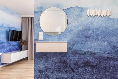 A bedroom with a modern design, featuring a round mirror, blue accents, and a stylish wall feature.
