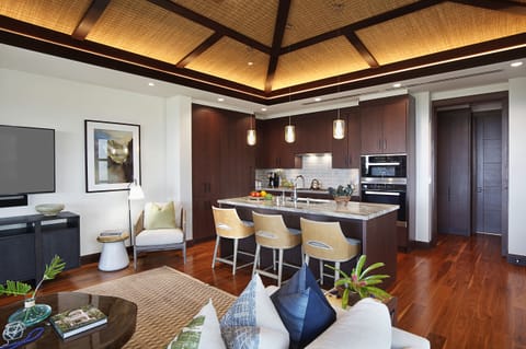 The home's polished ocean-view kitchen with gleaming granite counters, custom cabinetry, and large island with bar seating flows effortlessly into a sophisticated living space, which in turn flows out to a spacious covered lanai, blurring the lines between