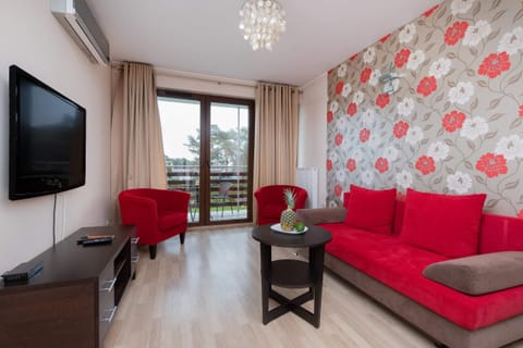 A cozy living room featuring a red armchair and a sofa, a wooden coffee table, and a TV mounted on the wall.