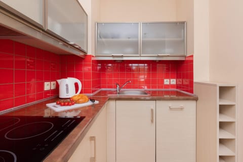 A modern kitchenette with red backsplash tiles, white cabinets, and appliances like a toaster and kettle.