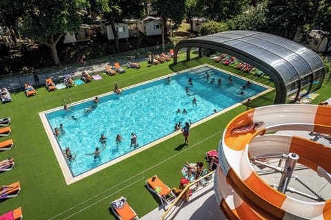 Guests enjoy a refreshing swim in the sunlit outdoor pool surrounded by loungers and lush greenery.