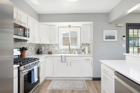 Modern kitchen with stainless steel appliances and gas range   - White cabinets with gold handles and geometric tile backsplash   - Bright space with window above sink for a home style feel