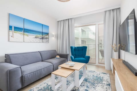 A bright living room with a comfortable grey sofa, a stylish blue armchair, and a coffee table by the window.

