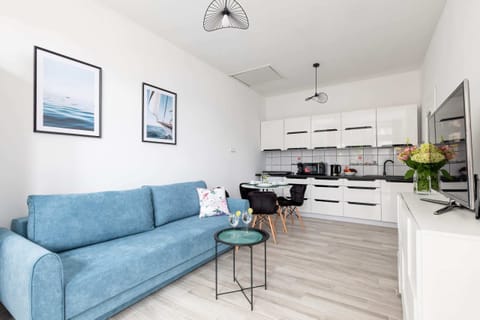 A bright living room with a blue sofa, coffee table, and an open layout connecting to the kitchen.