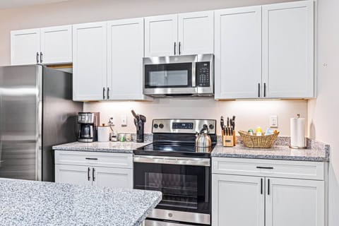 Step into our pristine, brand-new white kitchen featuring stainless steel appliances and a spacious island that seamlessly opens to the dining and living areas—ideal for your gatherings. ✨ #ModernLiving #HomeAwayFromHome