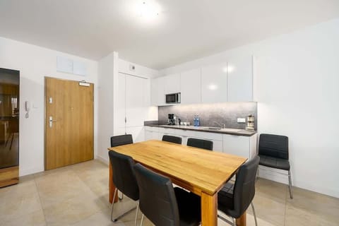 An open-plan living and dining area with a wooden table, white cabinets, and modern lighting, providing a spacious and inviting layout.