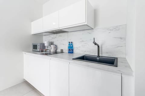 Another view of the kitchenette revealing a sleek sink area, marble-effect backsplash, and minimalist white cabinetry.