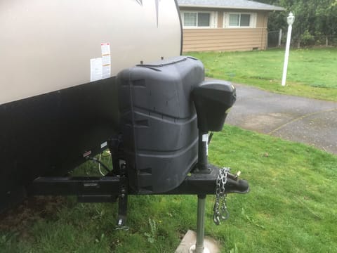 Electric tongue jack with two propane bottles under cover.